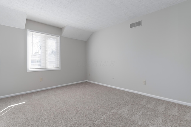 carpeted empty room with lofted ceiling, baseboards, visible vents, and a textured ceiling