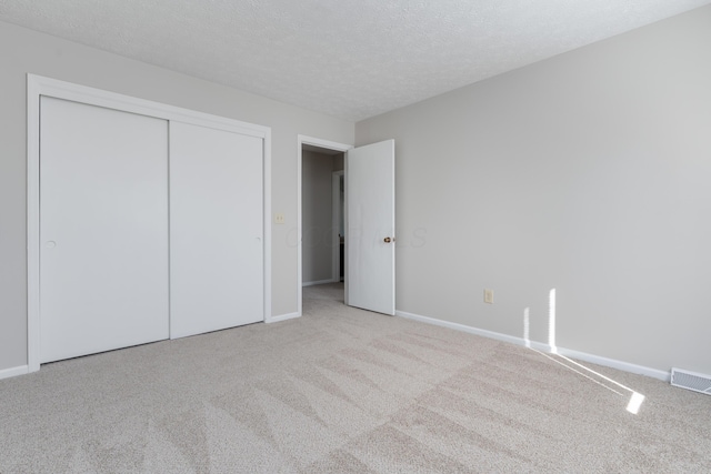 unfurnished bedroom featuring a textured ceiling, a closet, carpet flooring, and visible vents