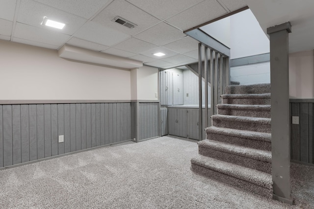 finished basement with visible vents, a drop ceiling, wainscoting, stairway, and carpet