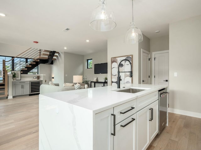 kitchen featuring sink, a center island with sink, beverage cooler, light hardwood / wood-style floors, and white cabinets