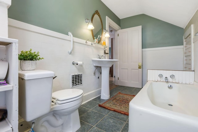 bathroom featuring tile patterned flooring, vaulted ceiling, wainscoting, a garden tub, and toilet