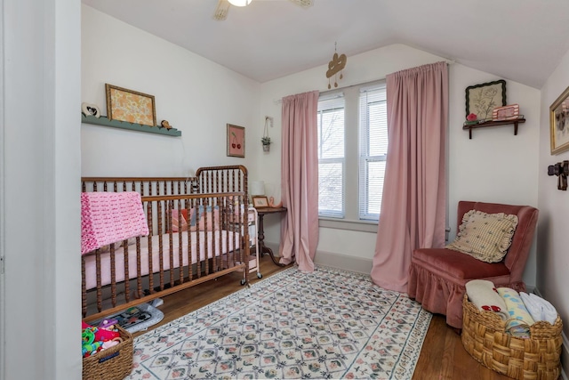 bedroom with lofted ceiling, a nursery area, wood finished floors, and baseboards