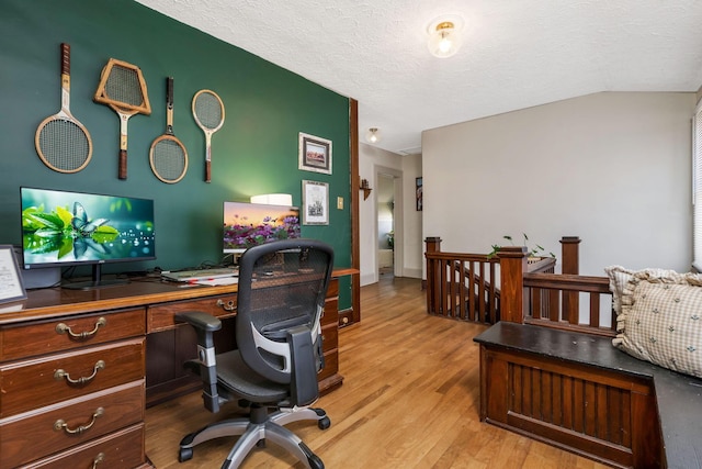 home office featuring vaulted ceiling, light wood-type flooring, and a textured ceiling