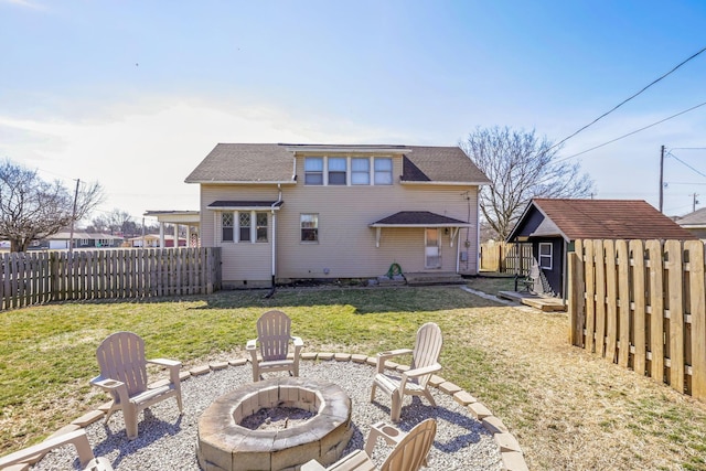 rear view of property featuring a fenced backyard, a shed, a yard, a fire pit, and an outdoor structure