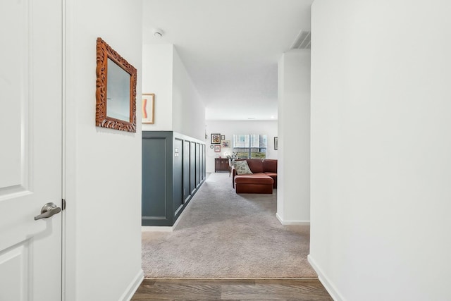 hallway featuring carpet, wood finished floors, visible vents, and baseboards