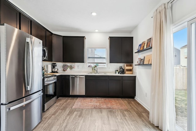 kitchen with appliances with stainless steel finishes, light countertops, dark brown cabinets, light wood-type flooring, and a sink