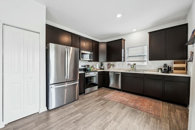 kitchen with stainless steel appliances, a sink, light wood-style floors, dark brown cabinets, and light countertops