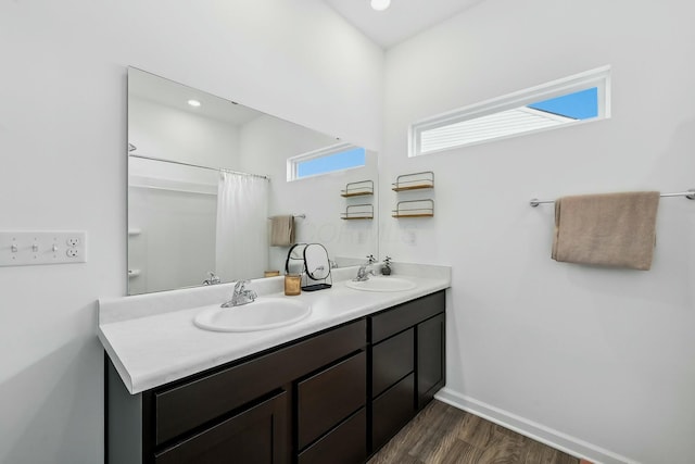 full bath with double vanity, a sink, baseboards, and wood finished floors