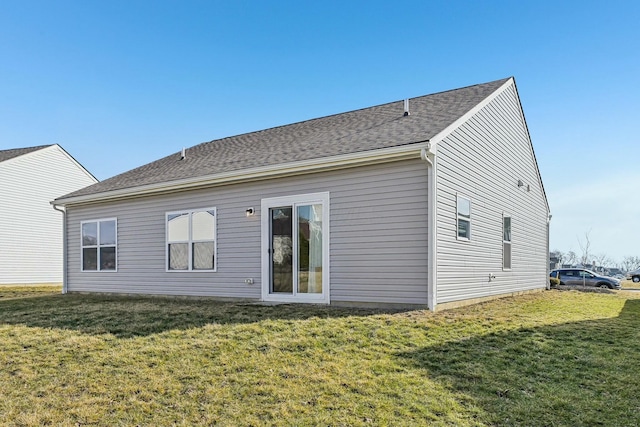 rear view of house featuring a shingled roof and a lawn