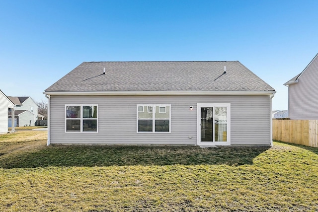 back of house with a shingled roof, fence, and a lawn