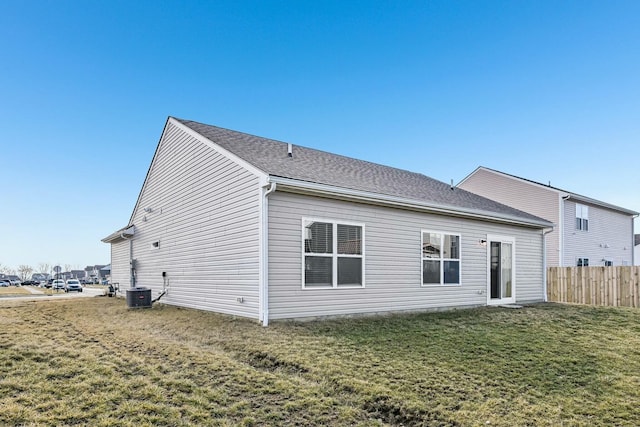 rear view of property with a shingled roof, central air condition unit, a lawn, and fence