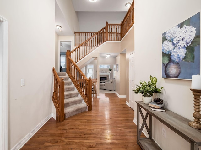 entrance foyer featuring a fireplace, a towering ceiling, and dark wood-type flooring