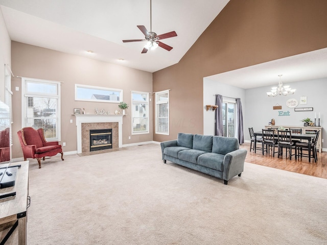 carpeted living room with high vaulted ceiling, a healthy amount of sunlight, ceiling fan with notable chandelier, and a fireplace