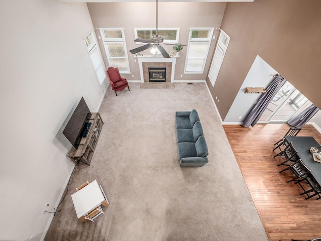 unfurnished living room featuring hardwood / wood-style flooring, ceiling fan, a towering ceiling, and a fireplace