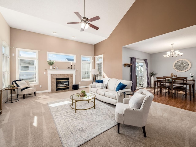 living room with baseboards, a tile fireplace, light colored carpet, a high ceiling, and ceiling fan with notable chandelier