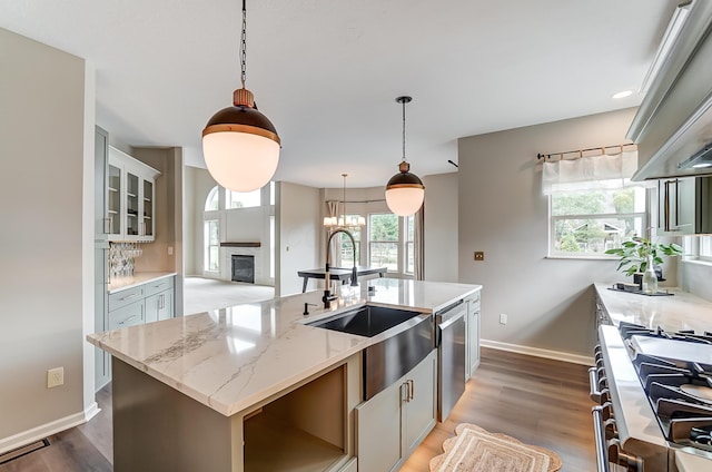 kitchen featuring light stone counters, stainless steel appliances, a kitchen island with sink, and hanging light fixtures