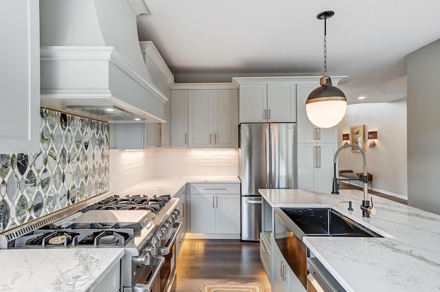 kitchen featuring sink, appliances with stainless steel finishes, premium range hood, hanging light fixtures, and light stone counters