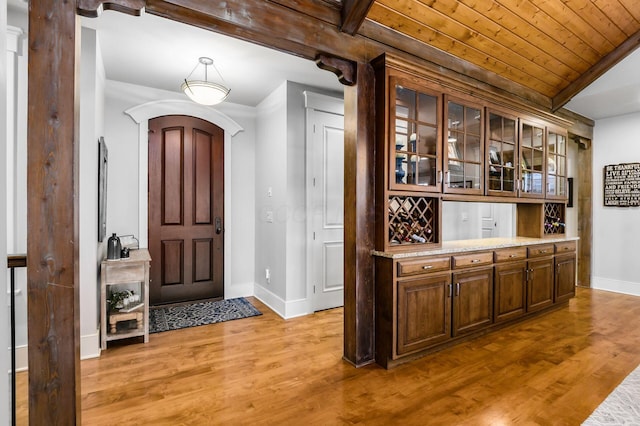 entryway with light wood-style flooring, lofted ceiling with beams, arched walkways, wooden ceiling, and baseboards