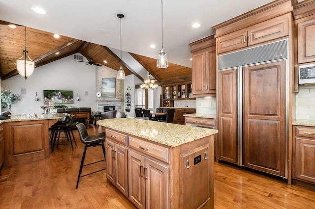 kitchen with paneled fridge, a large fireplace, light wood finished floors, and ceiling fan with notable chandelier