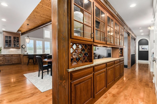 bar with arched walkways, backsplash, light wood finished floors, and pendant lighting