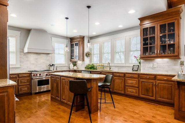 kitchen featuring light wood-type flooring, custom range hood, a sink, appliances with stainless steel finishes, and brown cabinetry