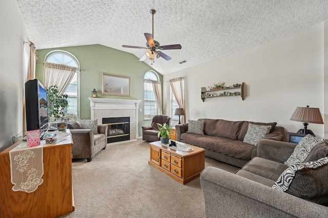 living room featuring a tiled fireplace, a ceiling fan, light colored carpet, vaulted ceiling, and a textured ceiling