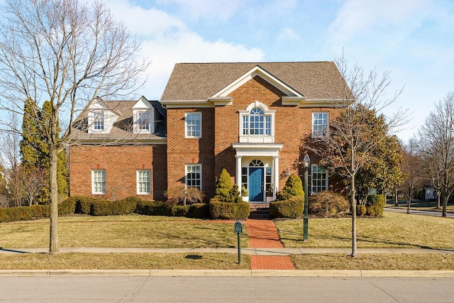 view of front of home featuring brick siding, a shingled roof, and a front yard