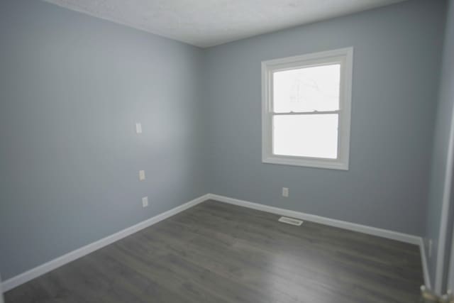 spare room featuring visible vents, baseboards, and dark wood-style flooring