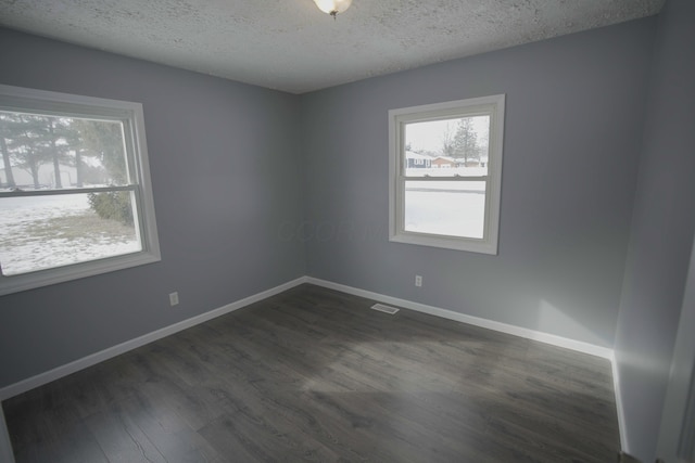 unfurnished room with visible vents, baseboards, a textured ceiling, and dark wood-style floors