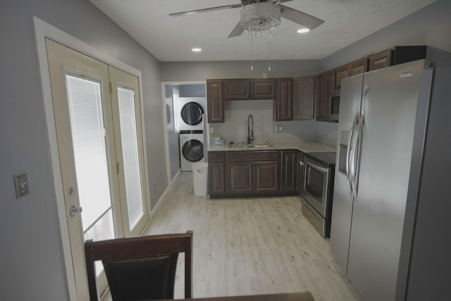 kitchen with light wood-style flooring, stacked washing maching and dryer, stainless steel appliances, a ceiling fan, and a sink