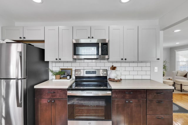 kitchen with white cabinetry, stainless steel appliances, dark brown cabinets, and decorative backsplash