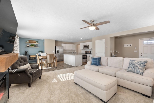 living room featuring light hardwood / wood-style floors, ceiling fan, and a textured ceiling