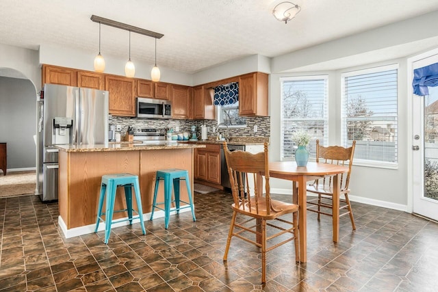 kitchen featuring a center island, arched walkways, tasteful backsplash, hanging light fixtures, and appliances with stainless steel finishes