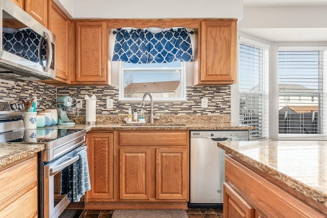 kitchen with a sink, appliances with stainless steel finishes, light stone countertops, tasteful backsplash, and brown cabinetry