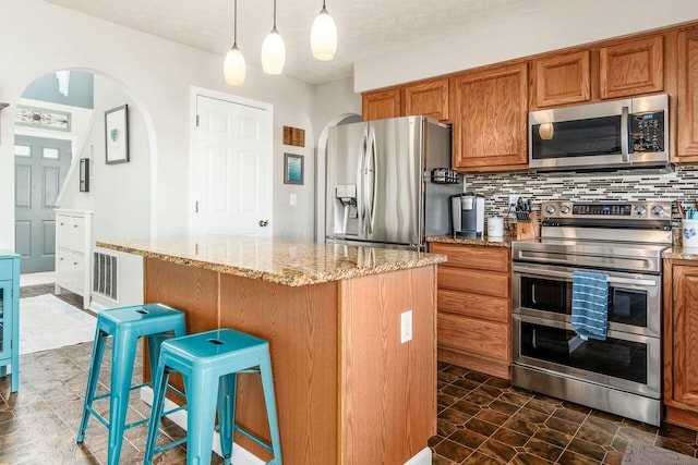 kitchen featuring light stone counters, brown cabinets, a breakfast bar area, hanging light fixtures, and stainless steel appliances