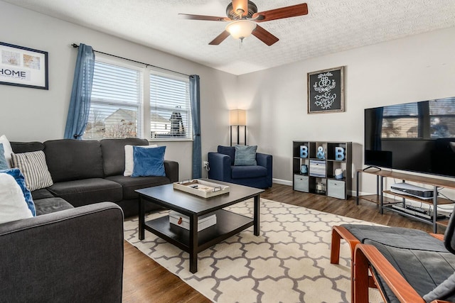 living room with ceiling fan, a textured ceiling, baseboards, and wood finished floors