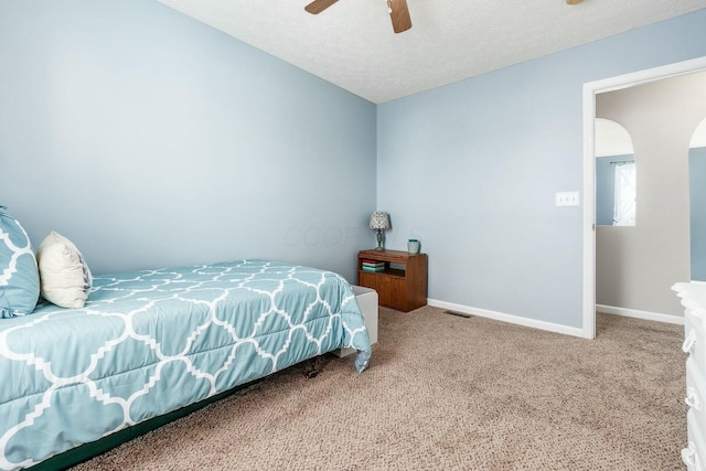 carpeted bedroom with baseboards, arched walkways, visible vents, ceiling fan, and a textured ceiling