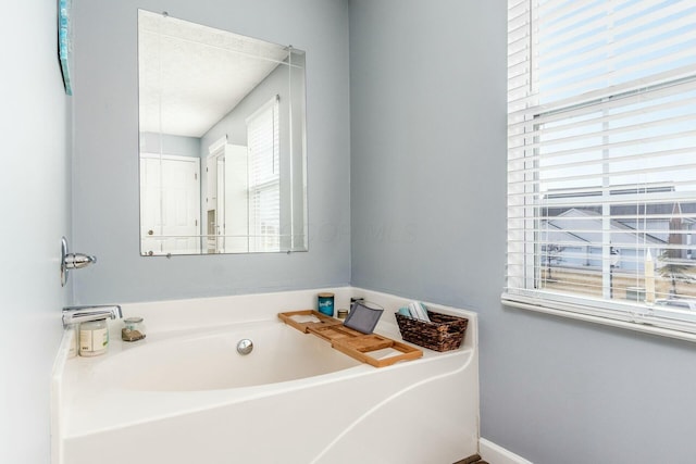 bathroom with a garden tub and baseboards