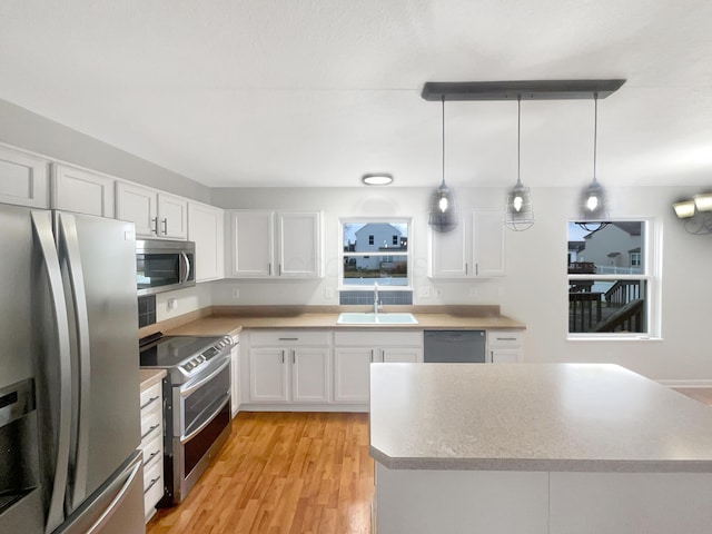 kitchen featuring appliances with stainless steel finishes, light hardwood / wood-style flooring, white cabinets, decorative light fixtures, and sink