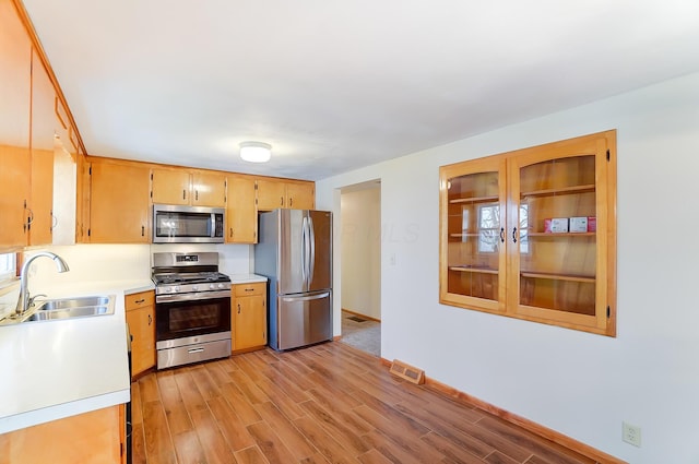 kitchen with appliances with stainless steel finishes, sink, and light hardwood / wood-style flooring