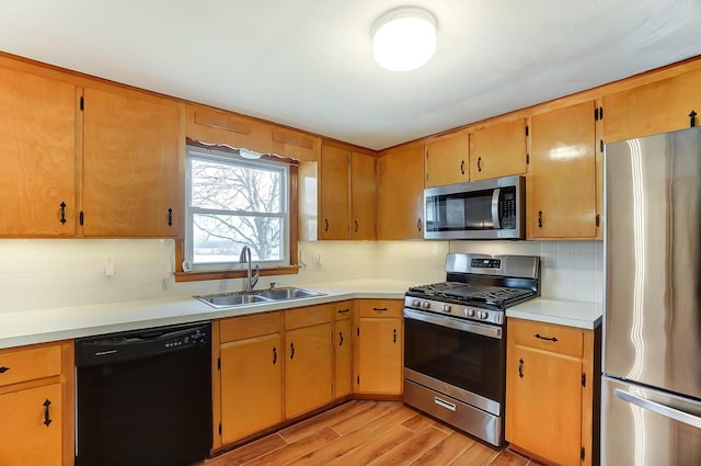 kitchen with stainless steel appliances, sink, backsplash, and light wood-type flooring