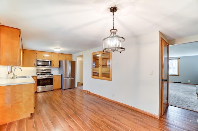 kitchen featuring stainless steel appliances, sink, light wood-type flooring, and decorative light fixtures