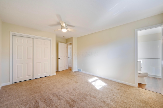 unfurnished bedroom featuring light carpet, a closet, ceiling fan, and ensuite bathroom