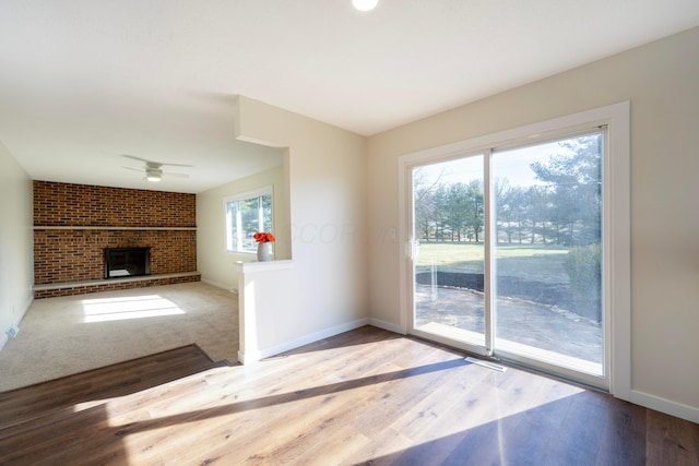 doorway with a brick fireplace, wood-type flooring, and ceiling fan