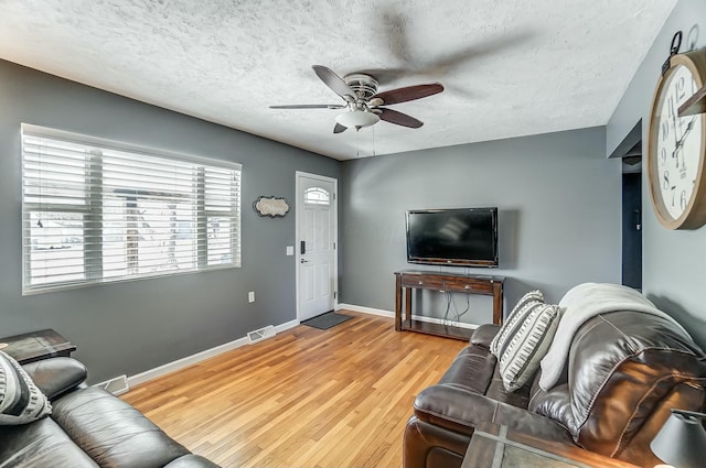 living room with ceiling fan, a textured ceiling, and light hardwood / wood-style floors