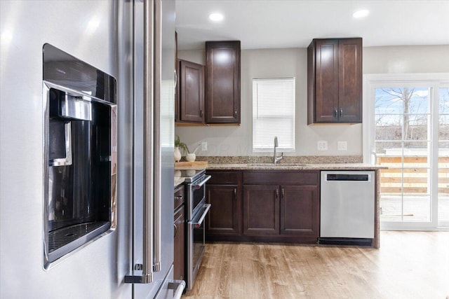 kitchen with light wood finished floors, appliances with stainless steel finishes, light stone countertops, dark brown cabinets, and a sink