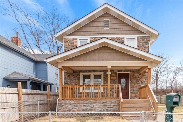 view of front of property featuring covered porch, stone siding, and a fenced front yard