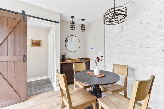 dining area with light wood-style floors, a barn door, brick wall, and baseboards