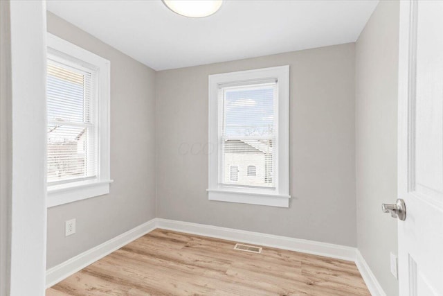 empty room with light wood-style floors, visible vents, and baseboards