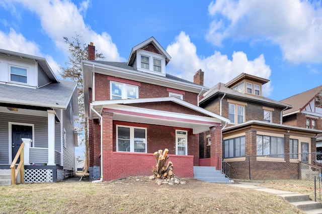 american foursquare style home with a chimney, a porch, and brick siding